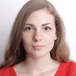A close-up portrait of a young woman with freckles, long hair, and a calm demeanor.
